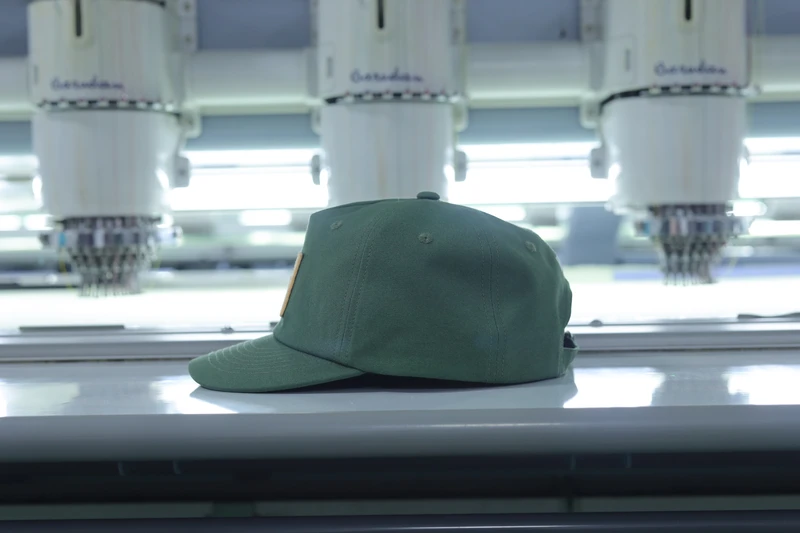 Plain olive baseball cap viewed from the side at an embroidery workstation