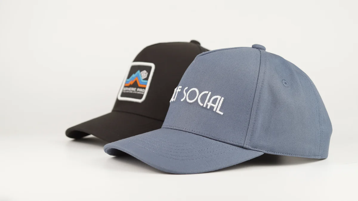 Grey script-embroidered cap beside a dark cap with a rectangular front patch