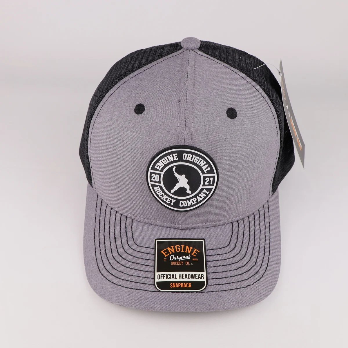 Front view of a grey trucker cap with circular embroidered badge and visor stitching