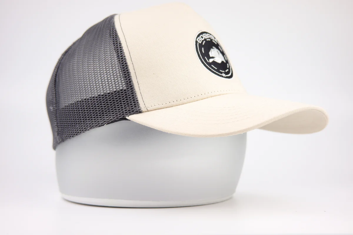 Cream round-patch trucker cap showing grey mesh panels from the front side