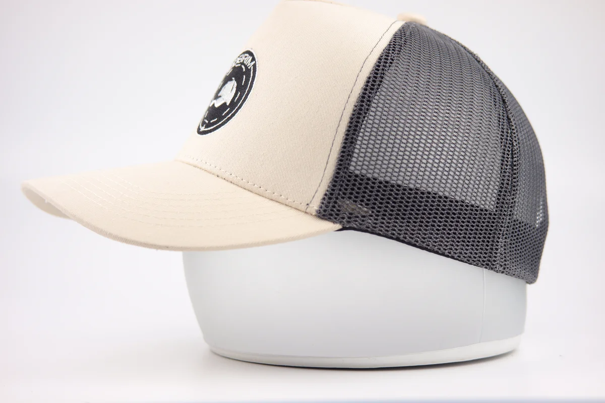 Opposite side of a cream round-patch trucker cap showing grey mesh and curved visor