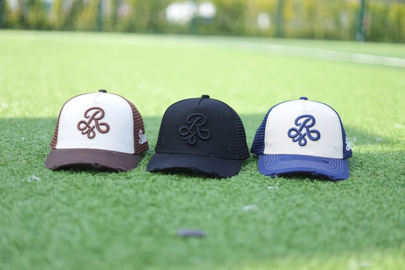 Three cream brown, black and navy monogram trucker caps on green sports turf