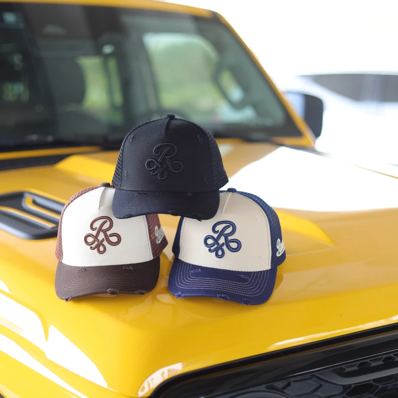 Brown, navy and black raised-monogram trucker caps styled on a yellow off-road vehicle