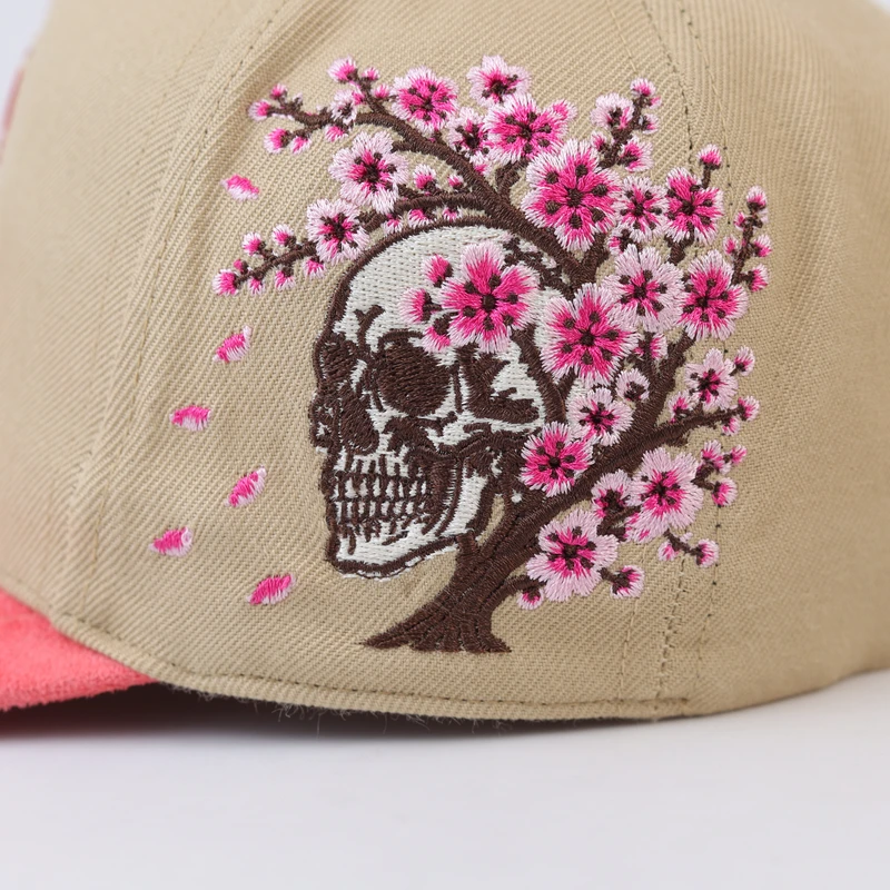 Close-up of pink blossom branches and skull motif embroidered on the khaki cap side panel